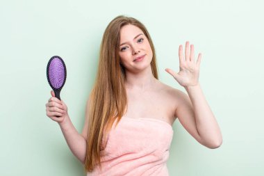 Kızıl saçlı kadın gülümsüyor ve arkadaş canlısı görünüyor, beş numarayı gösteriyor. saç tarağı konsepti