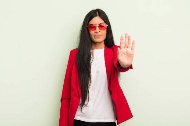 Genç, güzel, İspanyol bir kadın. Ciddi görünüyor. Avuç içi açık, dur hareketi yapıyor. İş kadını kavramı