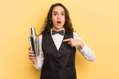 Şok olmuş ve ağzı açık, kendini işaret eden genç ve güzel İspanyol bir kadın. barmen ve kokteyl konsepti