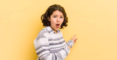 Oldukça İspanyol bir kadın şaşkın ve şaşırmış hissediyor. Yandaki fotokopi alanını işaret ediyor. Şaşırmış ve ağzı açık bakıyor.