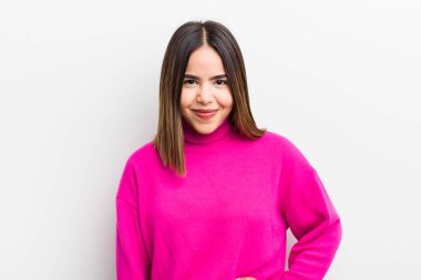 Güzel İspanyol kadın mutlu bir şekilde gülümsüyor, eli kalçasında ve kendinden emin, olumlu, gururlu ve arkadaş canlısı bir tavırla.