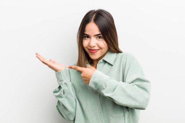 Güzel İspanyol kadın neşeyle gülümsüyor ve yan taraftaki fotokopi alanını işaret ederek bir nesneyi gösteriyor ya da reklamını yapıyor.