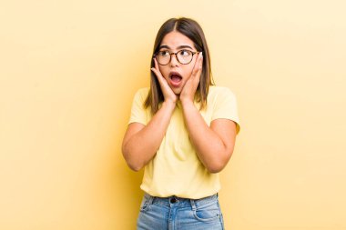 Güzel İspanyol bir kadın mutlu, heyecanlı ve şaşırmış hissediyor, iki eli yüzü üzerinde yana bakıyor.