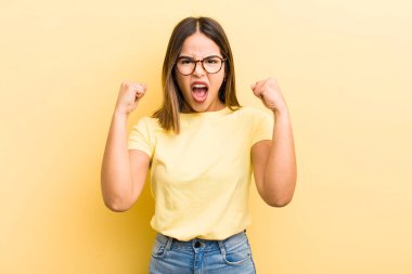 Güzel İspanyol bir kadın kızgın bir ifadeyle agresif bir şekilde bağırıyor ya da yumruklarıyla başarıyı kutluyor.