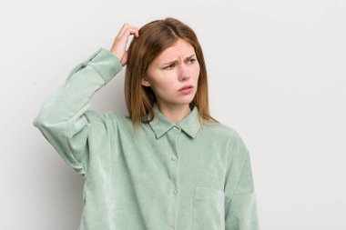 Kızıl saçlı güzel kadın şaşkın ve şaşkın hissediyor, kafasını kaşıyor ve yan tarafa bakıyor.