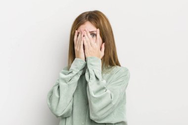 Kızıl saçlı güzel bir kadın elleriyle yüzünü kapatıyor, parmaklarının arasından şaşkın bir ifadeyle yan tarafa bakıyor.
