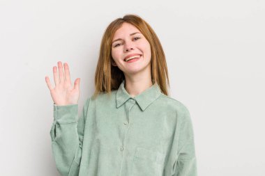 Kızıl saçlı güzel kadın mutlu ve neşeyle gülümsüyor, el sallıyor, seni selamlıyor ya da veda ediyor.