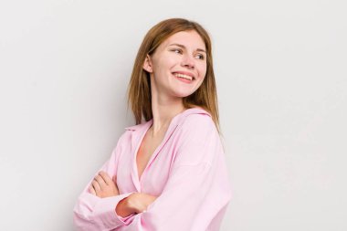 Kızıl saçlı güzel bir kadın neşeli bir şekilde gülümsüyor, mutlu, tatmin olmuş ve rahatlamış hissediyor, kollarını kavuşturup yan tarafa bakıyor.