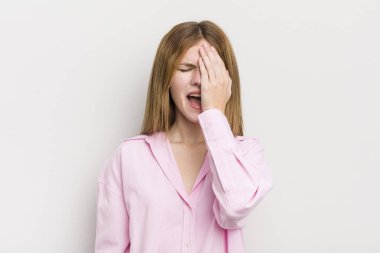 Kızıl saçlı güzel bir kadın uykulu, sıkılmış ve esniyor, baş ağrısı ve yüzünün yarısını kaplayan bir eliyle