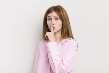 Kızıl saçlı güzel bir kadın sessizlik ve sessizlik istiyor, parmaklarıyla ağzının önünde işaret ediyor, 
