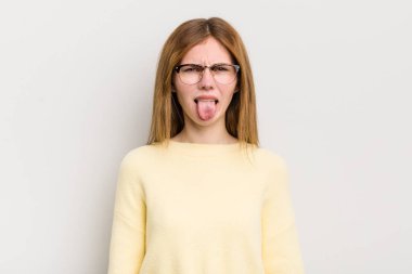 Kızıl saçlı güzel bir kadın tiksinmiş ve rahatsız olmuş hissediyor, dilini dışarı çıkarıyor, iğrenç ve iğrenç bir şeyden hoşlanmıyor.