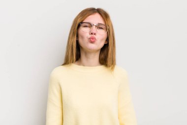 Kızıl saçlı güzel bir kadın tatlı, eğlenceli, mutlu, sevimli bir yüz ifadesiyle dudaklarını birbirine bastırıyor ve öpüşüyor.