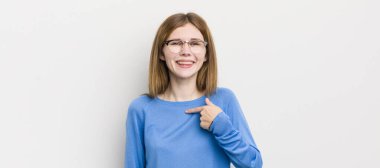 Kızıl saçlı güzel bir kadın mutlu, gururlu ve şaşırmış görünüyor, neşeli bir şekilde kendini gösteriyor, kendinden emin ve kibirli hissediyor.