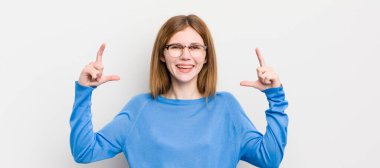 Kızıl saçlı güzel bir kadın iki eliyle kendi gülüşünü çiziyor, olumlu ve mutlu görünüyor, sağIık kavramı.