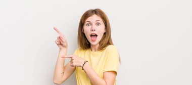 Kızıl saçlı güzel bir kadın, neşeli ve şaşırmış hissediyor, şok olmuş bir ifadeyle gülümsüyor ve yan tarafı işaret ediyor.