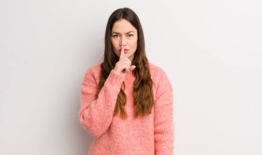 pretty caucasian woman looking serious and cross with finger pressed to lips demanding silence or quiet, keeping a secret