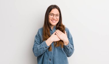 pretty caucasian woman feeling romantic, happy and in love, smiling cheerfully and holding hands close to heart