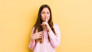 pretty caucasian woman looking serious and cross with finger pressed to lips demanding silence or quiet, keeping a secret