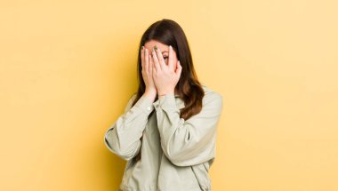 pretty caucasian woman feeling scared or embarrassed, peeking or spying with eyes half-covered with hands