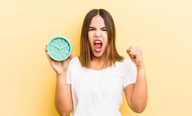 Güzel İspanyol kız sinirli bir ifadeyle agresif bir şekilde bağırıyor. Alarm saati kavramı