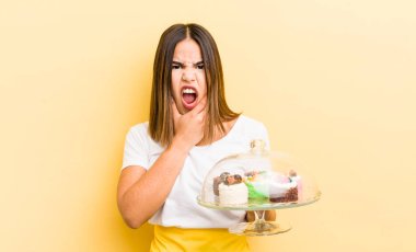 Ağzı ve gözleri sonuna kadar açık ve eli çenesinde güzel İspanyol bir kız. Ev yapımı kek konsepti