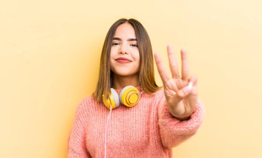 Güzel İspanyol kız gülümsüyor ve arkadaş canlısı görünüyor, üç numarayı gösteriyor. kulaklık konsepti