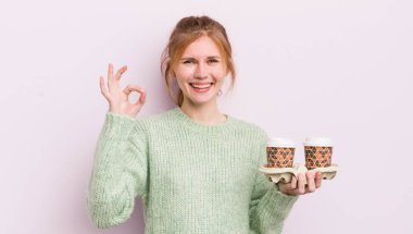 Kızıl saçlı güzel kız kendini mutlu hissediyor, iyi bir jestle onaylıyor. kahve konseptini kaldır.