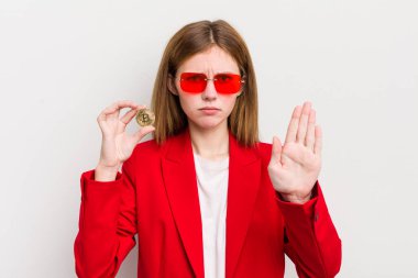 Kızıl saçlı güzel kız ciddi görünüyor. Avuç içini gösteriyor. Durdurma hareketi yapıyor. Bitcoin konsepti