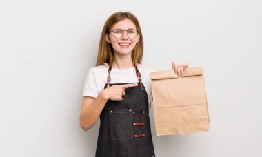 kızıl saçlı güzel kız neşeli bir şekilde gülümsüyor, mutlu hissediyor ve bir tarafı işaret ediyor. çalışanı götür.