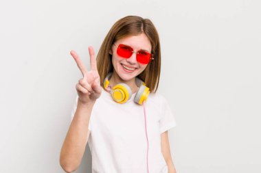 kızıl saçlı güzel kız gülümsüyor ve mutlu görünüyor, zafer ya da barış işareti yapıyor. müzik konseptini dinle