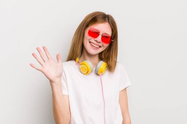 kızıl saçlı güzel kız gülümsüyor ve arkadaş canlısı görünüyor, beş numarayı gösteriyor. müzik konseptini dinle