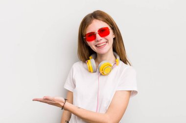kızıl saçlı güzel kız neşeli bir şekilde gülümsüyor, mutlu hissediyor ve bir konsept gösteriyor. müzik konseptini dinle