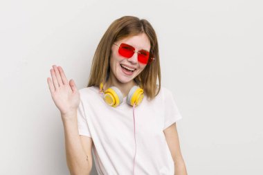 Kızıl saçlı güzel kız mutlu bir şekilde gülümsüyor, el sallıyor, seni selamlıyor ve selamlıyor. müzik konseptini dinle