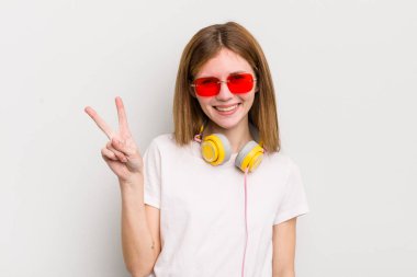 Kızıl saçlı güzel kız gülümsüyor ve arkadaş canlısı görünüyor. İki numarayı gösteriyor. müzik konseptini dinle