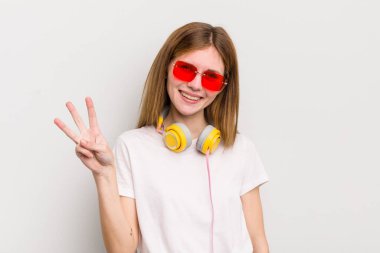 kızıl saçlı güzel kız gülümsüyor ve arkadaş canlısı görünüyor, üç numarayı gösteriyor. müzik konseptini dinle