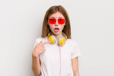 Kızıl saçlı güzel kız şok olmuş ve ağzı açık, kendini işaret eden bir şekilde şaşırmış görünüyor. müzik konseptini dinle