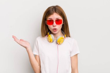 Kızıl saçlı güzel kız şaşırmış ve şok olmuş görünüyor. Çenesi düşmüş ve elinde bir nesne var. müzik konseptini dinle