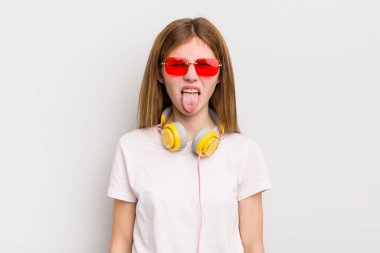 Kızıl saçlı güzel kız iğrenmiş ve sinirlenmiş hissediyor ve dilini dışarı çıkarıyor. müzik konseptini dinle