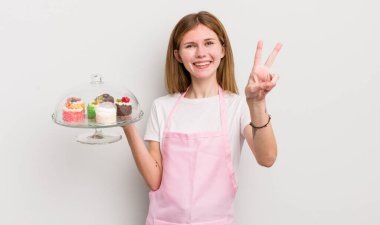 kızıl saçlı güzel kız gülümsüyor ve mutlu görünüyor, zafer ya da barış işareti yapıyor. Ev yapımı kek konsepti