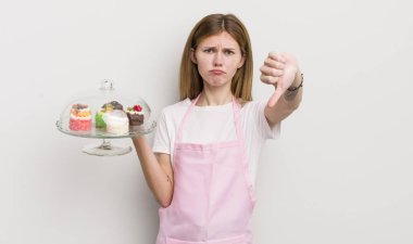 Kızıl saçlı güzel kız kendini kötü hissediyor, baş parmağını kaldırıyor. Ev yapımı kek konsepti