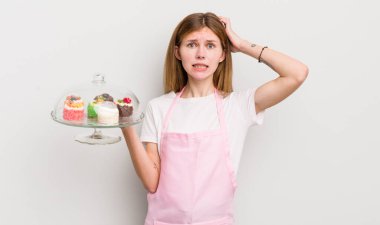 Kızıl saçlı güzel kız stresli, endişeli ya da korkmuş, elleri başının üstünde. Ev yapımı kek konsepti