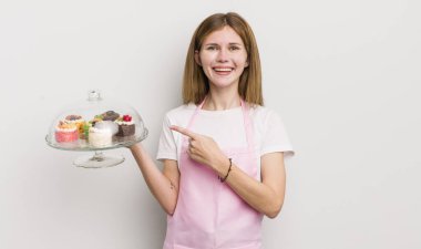 kızıl saçlı güzel kız neşeli bir şekilde gülümsüyor, mutlu hissediyor ve bir tarafı işaret ediyor. Ev yapımı kek konsepti