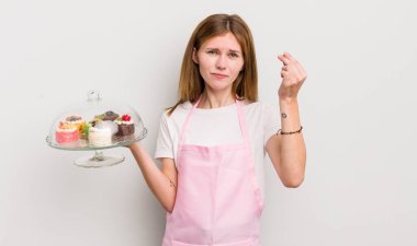 Kızıl saçlı güzel kız kapiş ya da para hareketi yapıyor, sana ödemeni söylüyor. Ev yapımı kek konsepti