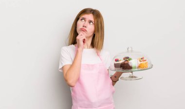 Kızıl saçlı güzel kız düşünüyor, kuşkulu ve şaşkın hissediyor. Ev yapımı kek konsepti