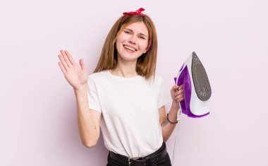 Kızıl saçlı güzel kız mutlu bir şekilde gülümsüyor, el sallıyor, seni selamlıyor ve selamlıyor. kahya konsepti