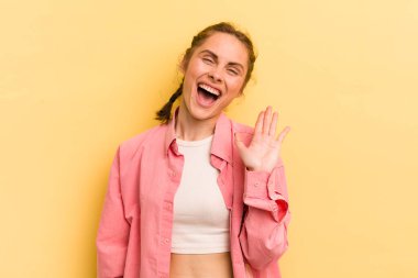 Genç ve güzel bir kadın mutlu ve neşeyle gülümsüyor, el sallıyor, sizi selamlıyor ve selamlıyor, ya da veda ediyor.