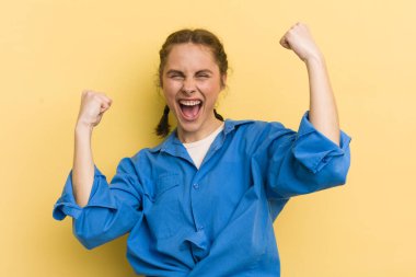 Genç ve güzel bir kadın muzaffer bir şekilde bağırıyor. Heyecanlı, mutlu ve şaşırmış görünüyor. Kutlama yapıyor.