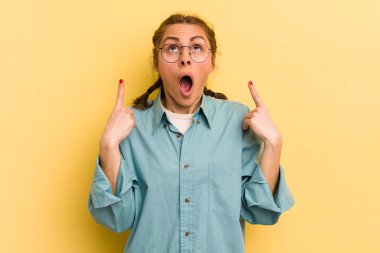 Genç ve güzel bir kadın huşu içinde ve ağzı açık bir şekilde şaşkın ve şaşkın bir bakışla yukarıya bakıyor.