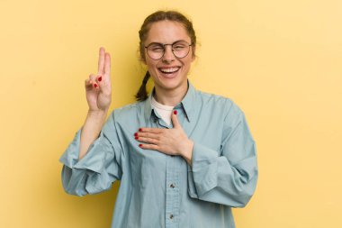 Genç, güzel bir kadın mutlu, kendinden emin ve güvenilir görünüyor. Gülümsüyor ve zafer işareti gösteriyor. Olumlu bir tavırla.