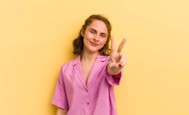 Genç, güzel bir kadın gülümsüyor ve arkadaş canlısı görünüyor. İki ya da iki numarayı gösteriyor. Elleri önde, geri sayıyor.